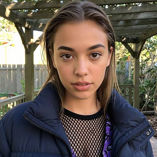 Photograph of a young woman with light brown skin, straight brown hair, and brown eyes, wearing a black puffer jacket over a fishnet top