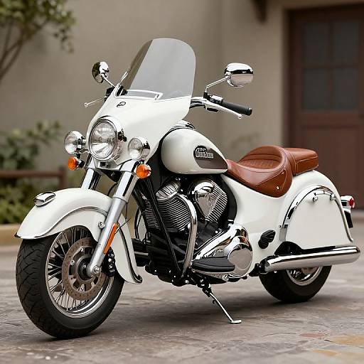 Photograph of a white cruiser motorcycle with brown leather seat, chrome details, clear windscreen, and orange headlights, parked on a cobblestone street