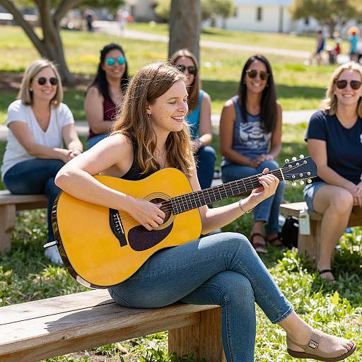Photograph of a smiling young woman with long brown hair, playing a yellow acoustic guitar on a wooden bench in a sunny park, with five seated women