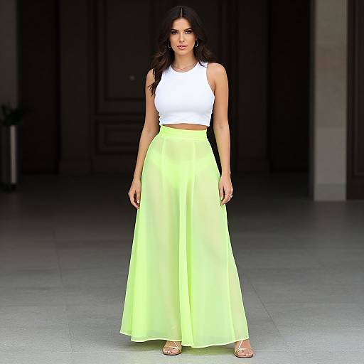 Photograph of a dark-haired woman in a white sleeveless crop top and high-waisted, bright yellow, flowing skirt, standing on a gray