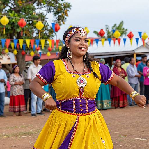 Photograph of a smiling Indian woman in a vibrant yellow and purple traditional dress, adorned with jewelry, dancing outdoors at a colorful festival with flags and a