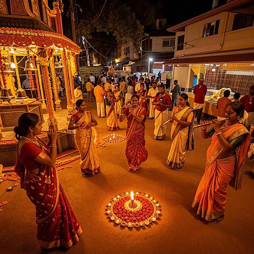 Nighttime photograph of Indian women in colorful traditional saris performing a ritual around a lit flower mandala, surrounded by a crowd in a street festival setting