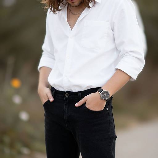 Photograph of a woman with shoulder-length brown hair, wearing a white button-up shirt, black jeans, and a black wristwatch, standing outdoors with