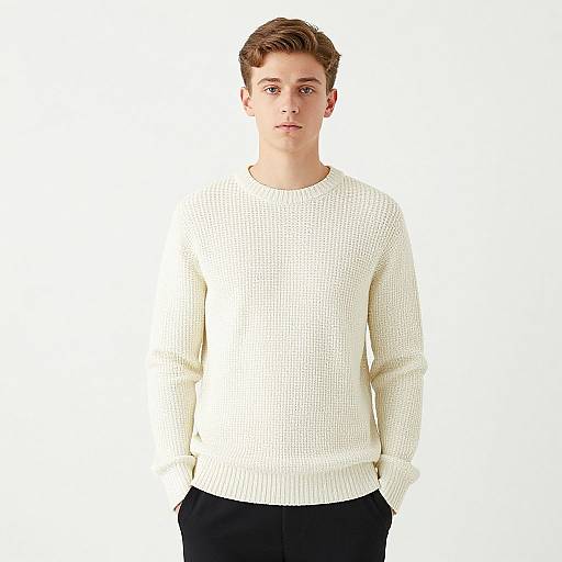Photograph of a young, fair-skinned man with short brown hair, wearing a white knit sweater and black pants, standing against a plain white background