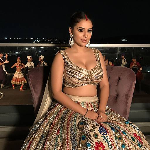Photograph of a South Asian woman in a sparkling, gold and sequin lehenga, sitting on a rooftop at night, surrounded by dancers.