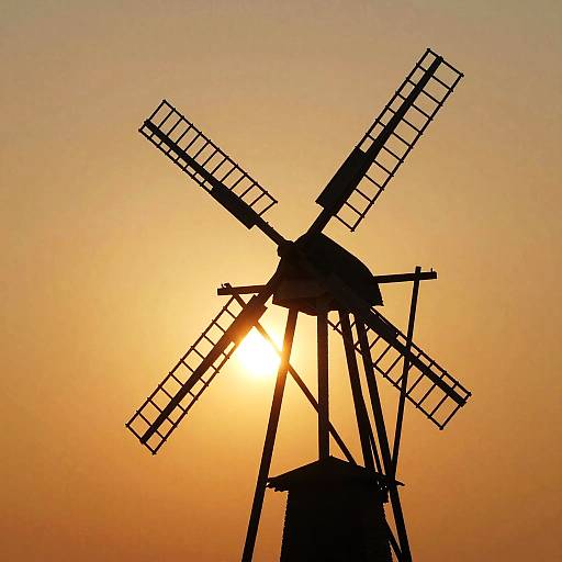 Silhouetted windmill with four blades against a vibrant orange sunset, creating a striking contrast and beautiful, warm gradient background.
