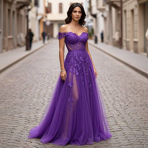 Photograph of a woman with dark, wavy hair in an off-shoulder, purple lace and tulle gown standing on a cobblestone