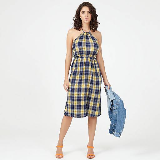 Photograph of a curvy woman with wavy dark hair, wearing a blue-yellow plaid halter dress, holding a denim jacket, and orange