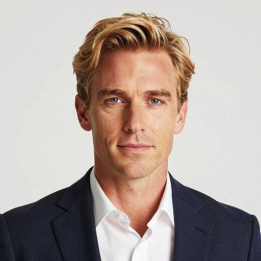Photograph of a handsome, blonde-haired man with blue eyes, wearing a black suit and white shirt, against a plain white background.