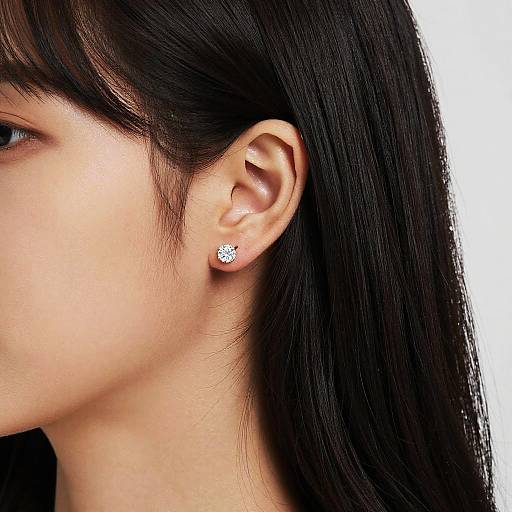 Close-up photograph of an Asian woman's ear with long black hair, wearing a single diamond stud earring, against a white background.