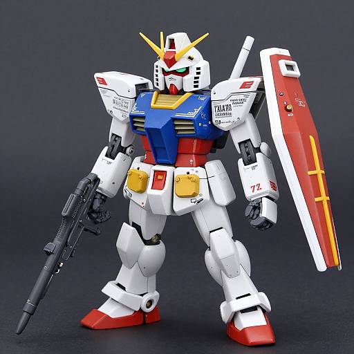Photograph of a detailed, white, red, and blue Gundam-style robot with yellow head crest, holding a gun in left hand and a large red