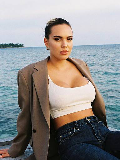 Photograph of a confident woman with tan skin and dark hair, wearing a brown blazer, white crop top, and high-waisted jeans,