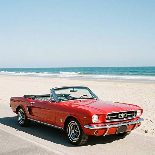 Photograph of a vibrant red vintage convertible car with chrome details parked on a sunny beach, ocean waves and clear blue sky in the background.