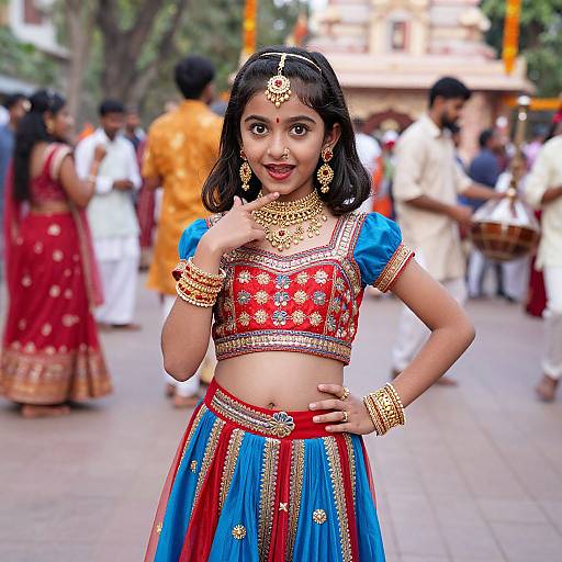 Photograph of a young Indian woman in traditional attire, wearing a red and blue embroidered crop top and skirt, gold jewelry, and a headpiece,