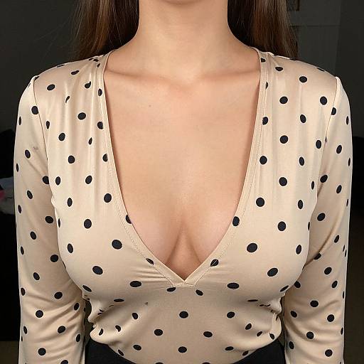 Photograph of a woman's chest and upper torso wearing a beige, long-sleeve, deep V-neck polka dot top, highlighting cleavage