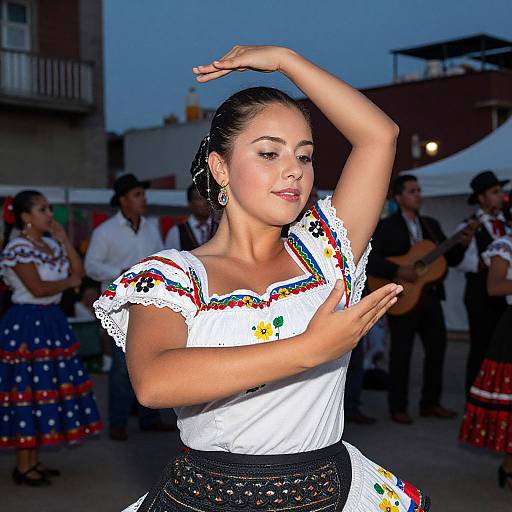 Photograph of a Latina woman in a white embroidered dress, black belt, and silver earrings, dancing with raised arms at dusk, surrounded by other dancers
