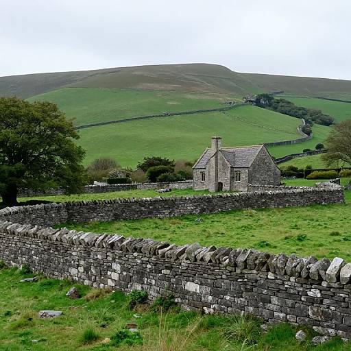 Photograph of a quaint, stone cottage with grey slate roof, set in lush green countryside, surrounded by dry stone walls, and rolling hills in the