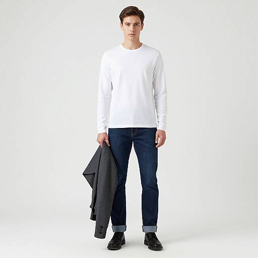 Photograph of a young man with short brown hair, wearing a white long-sleeve shirt, dark blue jeans, black shoes, holding a black