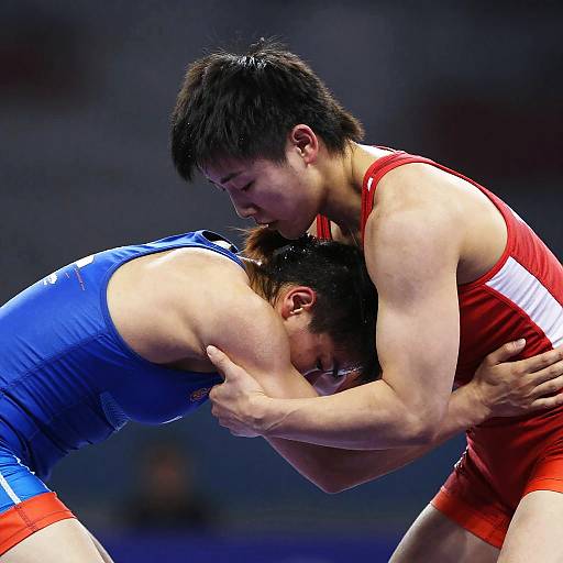 Photograph of two male wrestlers in action, one in a blue singlet and the other in a red singlet, grappling intensely, heads pressed together