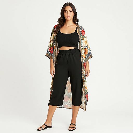 Photograph of a woman with long dark hair, wearing a colorful floral kimono, black crop top, and black capri pants, standing against a