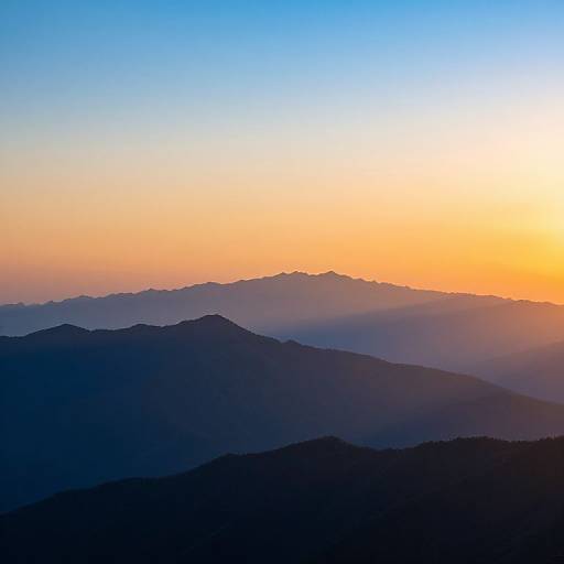 Photograph of a serene mountain landscape at sunrise, featuring layered blue and purple silhouetted mountain ranges under a gradient sky of orange and blue.