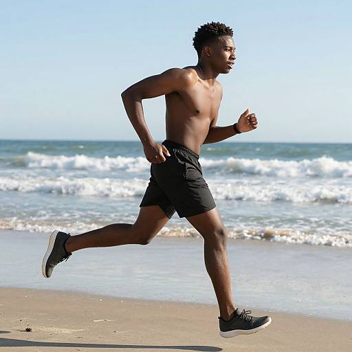Photograph of a fit, shirtless Black man jogging on a sunny beach, wearing black shorts and black sneakers, with ocean waves in the background.