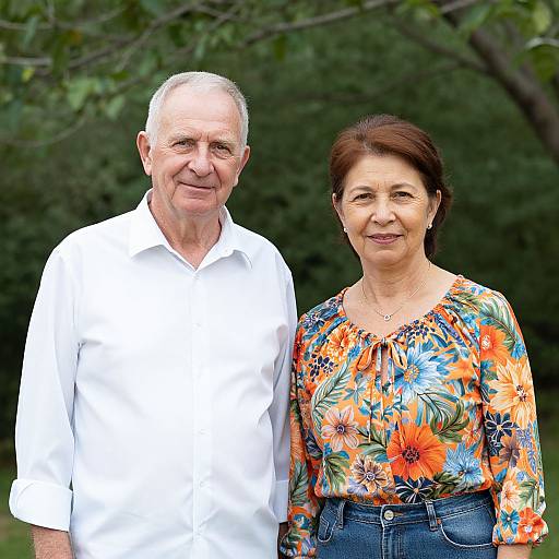 Photograph of an elderly white couple standing outdoors; the man in a white shirt, the woman in a floral blouse and jeans.