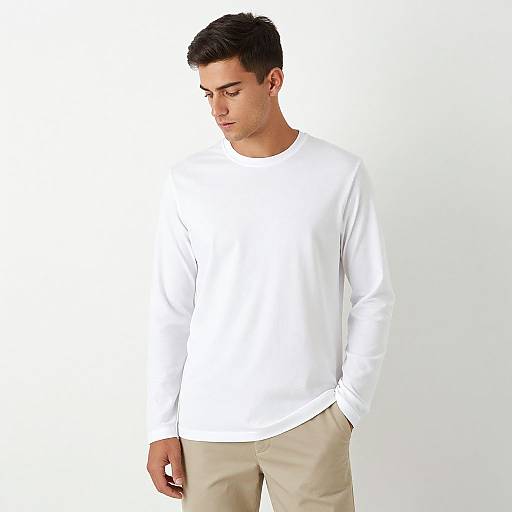 Photograph of a young man with short dark hair, wearing a plain white long-sleeve shirt and beige pants, looking down against a white background