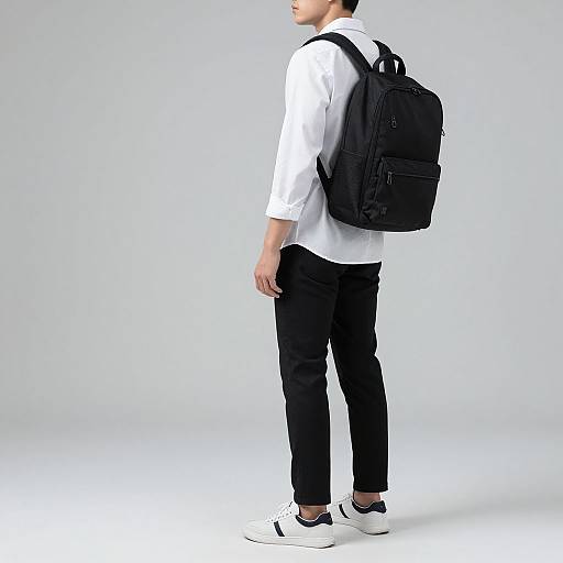 Photograph of a young man in a white shirt, black pants, white sneakers, and a black backpack, standing against a plain white background.