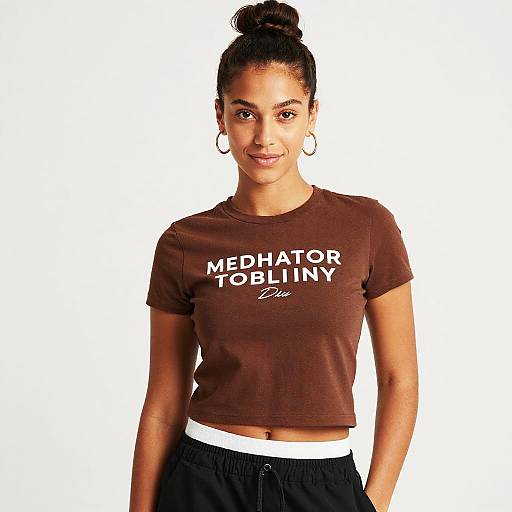 Photograph of a smiling young woman with dark skin, black hair in a bun, wearing a brown 