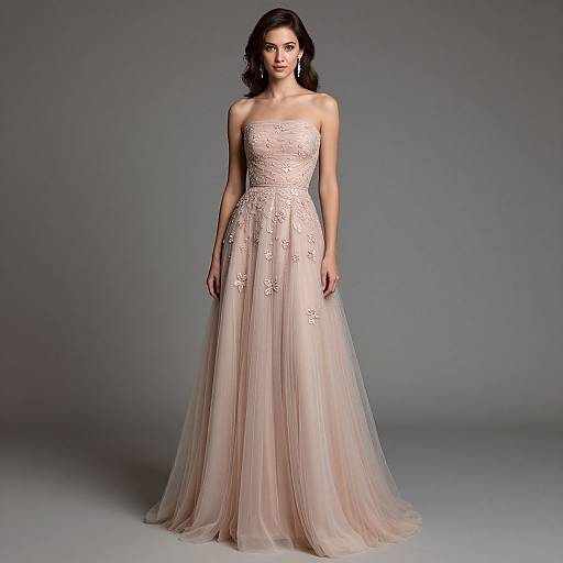 Photograph of a brunette woman in a strapless, pale pink, lace-embellished, full-length, tulle ball gown, standing against