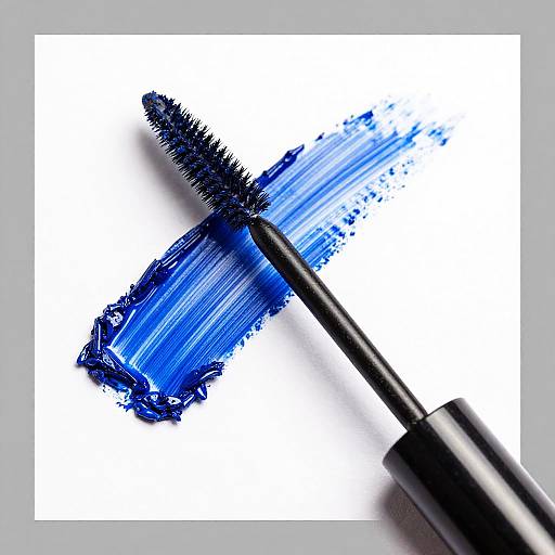 Photograph of a black mascara wand with thick blue mascara brush strokes on a white background, highlighting vibrant blue color and texture.