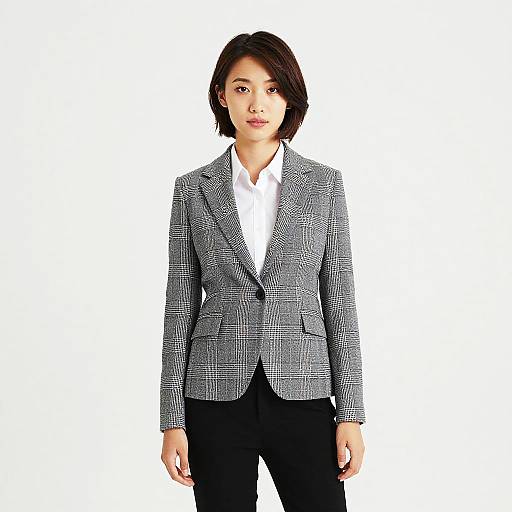 Photograph of an Asian woman with short black hair, wearing a grey plaid blazer over a white shirt and black pants, standing against a plain