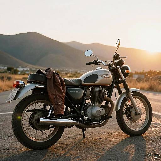 Photograph of a vintage Suzuki motorcycle with brown jacket draped over the seat, parked on a sunlit mountain road at sunset.