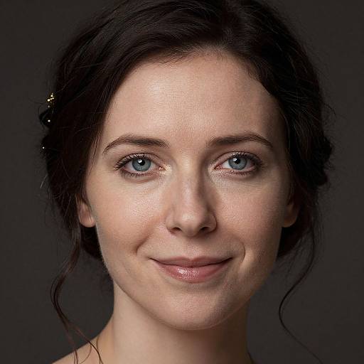Close-up photograph of a fair-skinned, blue-eyed woman with dark brown hair, slight smile, minimal makeup, against a dark background.