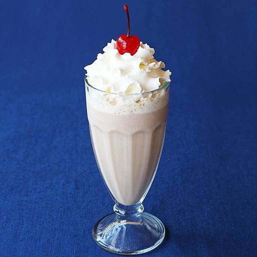 Photograph of a glass dessert cup with creamy vanilla pudding, topped with whipped cream and a red cherry, set against a deep blue background.