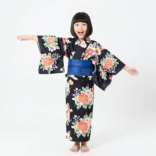 Photograph of a smiling Asian woman with a black bob haircut, wearing a black floral kimono with a blue obi, standing barefoot against a