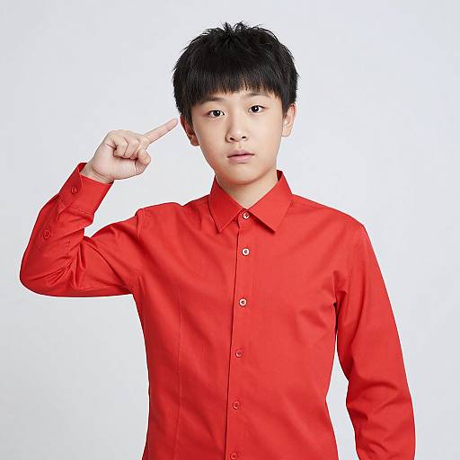 Photograph of an Asian man with short black hair, wearing a bright red button-down shirt, pointing to his forehead with his right index finger against a