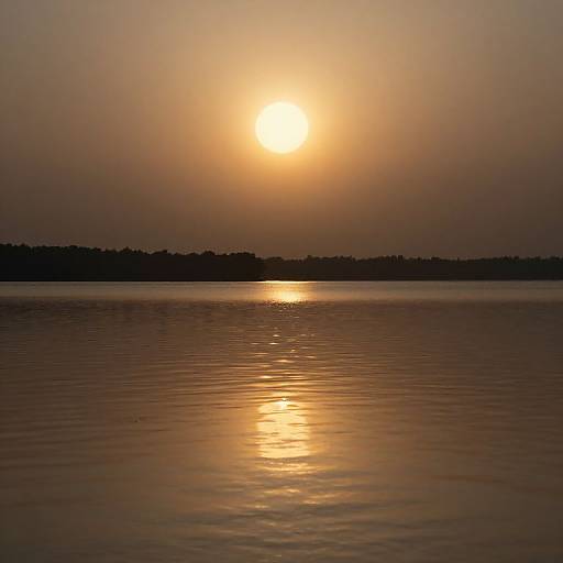 Photograph of a serene sunset over a calm lake, with the sun glowing orange, casting a golden reflection on the water. Silhouetted distant