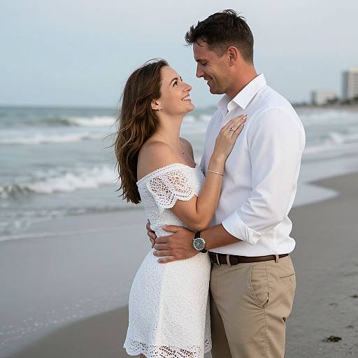 Photograph of a smiling couple on a beach, the woman in a white off-shoulder lace dress, the man in a white shirt and kh