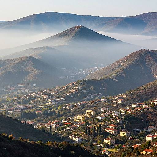 Photograph of a misty mountain town with red-roofed buildings, lush greenery, and hilly landscapes in the background, bathed in