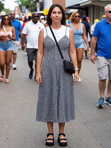Photograph of a woman in a black-and-white checkered dress, black sandals, and black crossbody bag, walking in a busy urban street with