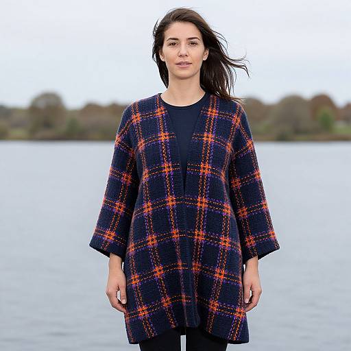 Photograph of a woman with long dark hair, wearing a black plaid dress with orange lines, standing in front of a calm lake.