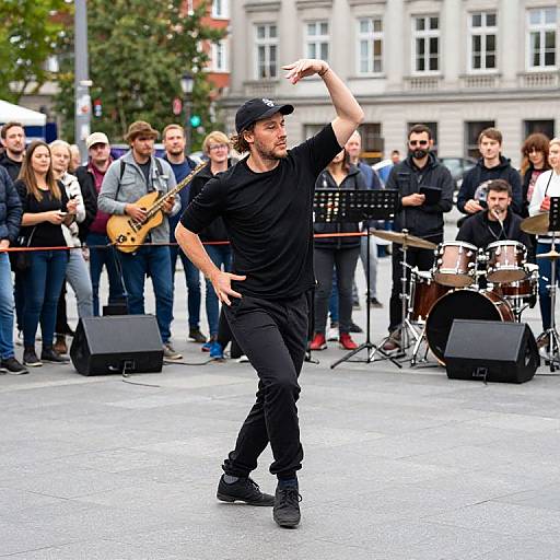 Photograph: Male street performer in black outfit and cap, playing electric guitar, dancing in front of a live band and cheering crowd in urban square.