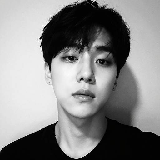 Black and white photograph of an Asian man with short, messy black hair, wearing a dark shirt, against a plain white background. His expression is neutral