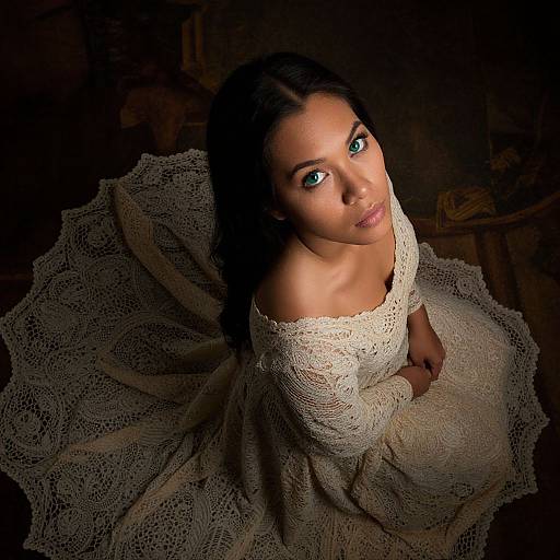 Photograph of a woman with striking green eyes, dark hair, and fair skin, wearing an off-shoulder, lace, cream-colored dress,