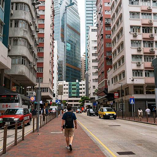 Photograph of a bustling urban street in a Chinese city, featuring a man in a blue shirt and khaki shorts walking away, surrounded by tall buildings