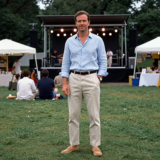 Photograph of a smiling, medium-built man with short brown hair, wearing a light blue button-up shirt, beige pants, and tan shoes, standing
