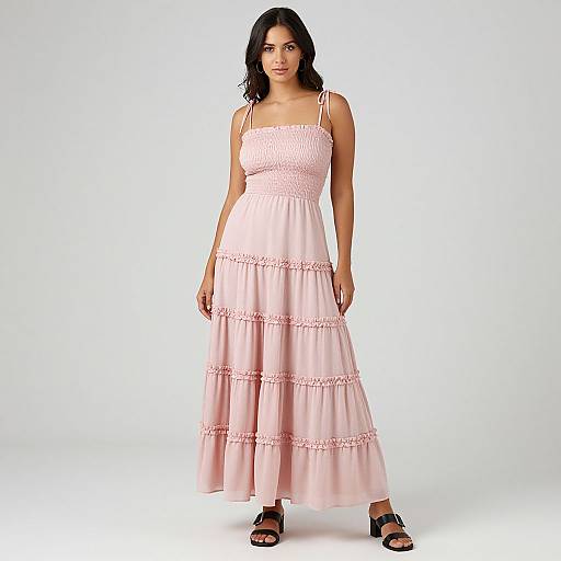 Photograph of a brunette woman with medium skin tone, wearing a pink, sleeveless, layered maxi dress with lace trim, and black sandals, standing