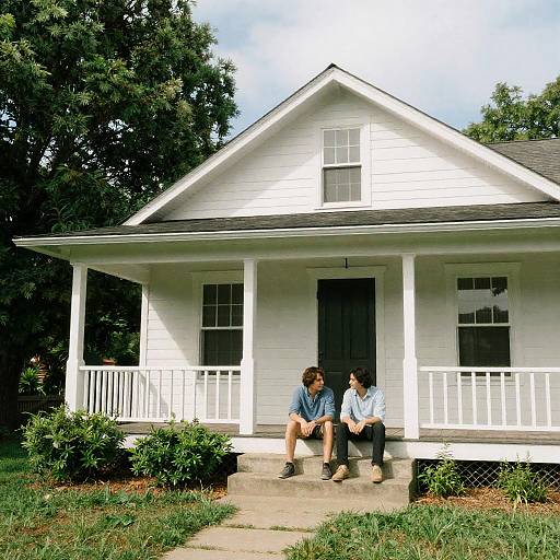 Two People Sitting on Porch Steps of White Wooden House